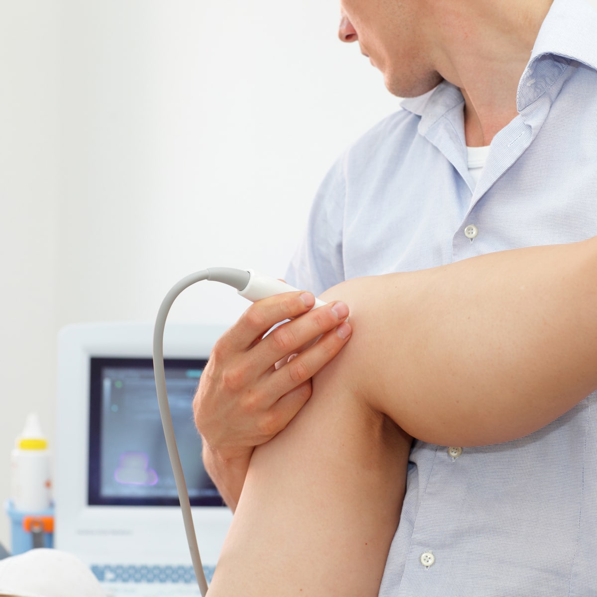 Im Ortho Health Institut in München führt ein Arzt eine Ultraschalluntersuchung am Knie eines Patienten durch. Der Arzt hält die Ultraschallsonde in der Hand, im Hintergrund ist ein Monitor zu sehen, auf dem die Bildergebnisse angezeigt werden.