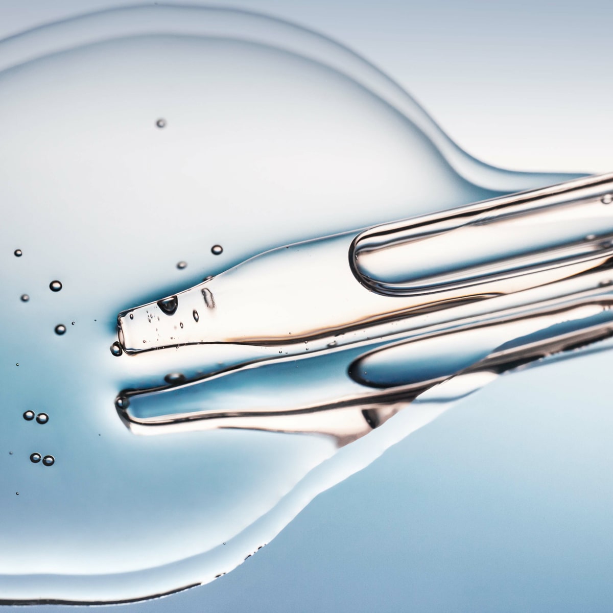 © Ortho Health Institut in München Nahaufnahme einer klaren, viskosen Flüssigkeit mit Blasen, hervorgehoben vor einem hellblauen Hintergrund im Ortho Health Institut in München. Die Flüssigkeit scheint in Bewegung zu sein, mit glatten, fließenden Linien und unterschiedlicher Dicke. Die Komposition ist abstrakt und hat eine glänzende, reflektierende Qualität.